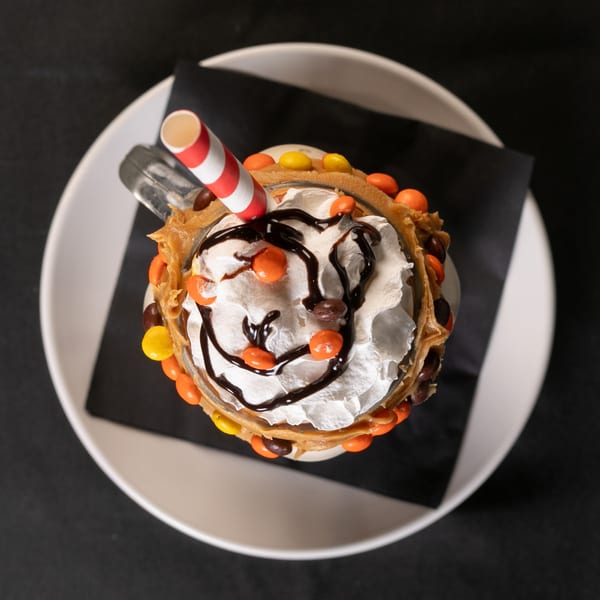 Overhead view of a Roadhouse milkshake with whipped cream, chocolate drizzle, and candies.