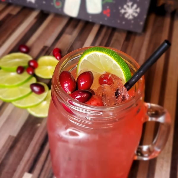 A Roadhouse cranberry cocktail in a mason jar, garnished with lime, cranberries, and a black straw.