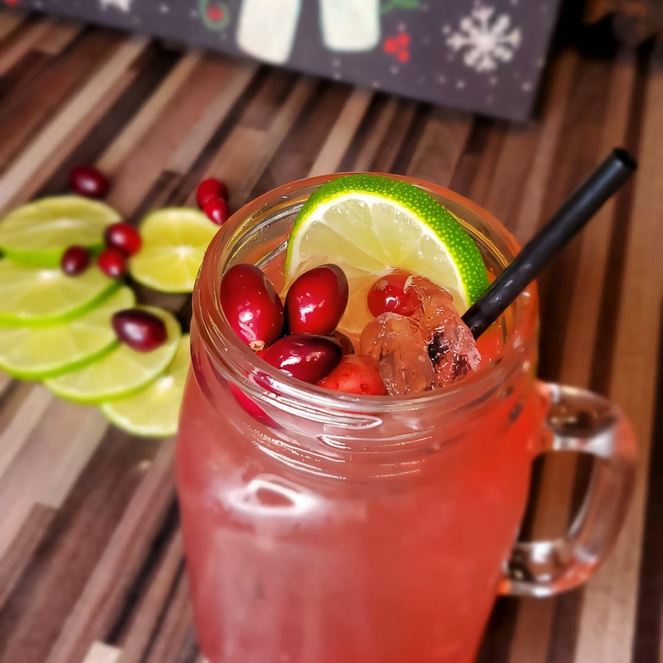 A Roadhouse cranberry cocktail in a mason jar, garnished with lime, cranberries, and a black straw.