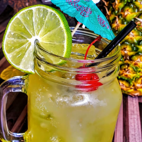 A Roadhouse sports-bar cocktail in a mason jar with lime, cherry, umbrella, and straw.