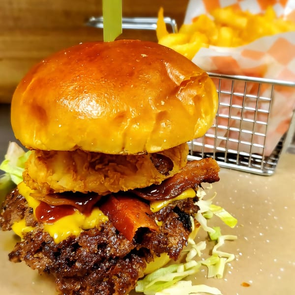 A Roadhouse burger with bacon, cheese, onion rings, and lettuce, served with fries.