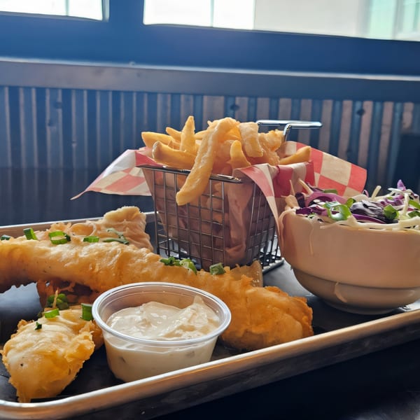 The Roadhouse's fish and chips with coleslaw and tartar sauce on a metal tray.